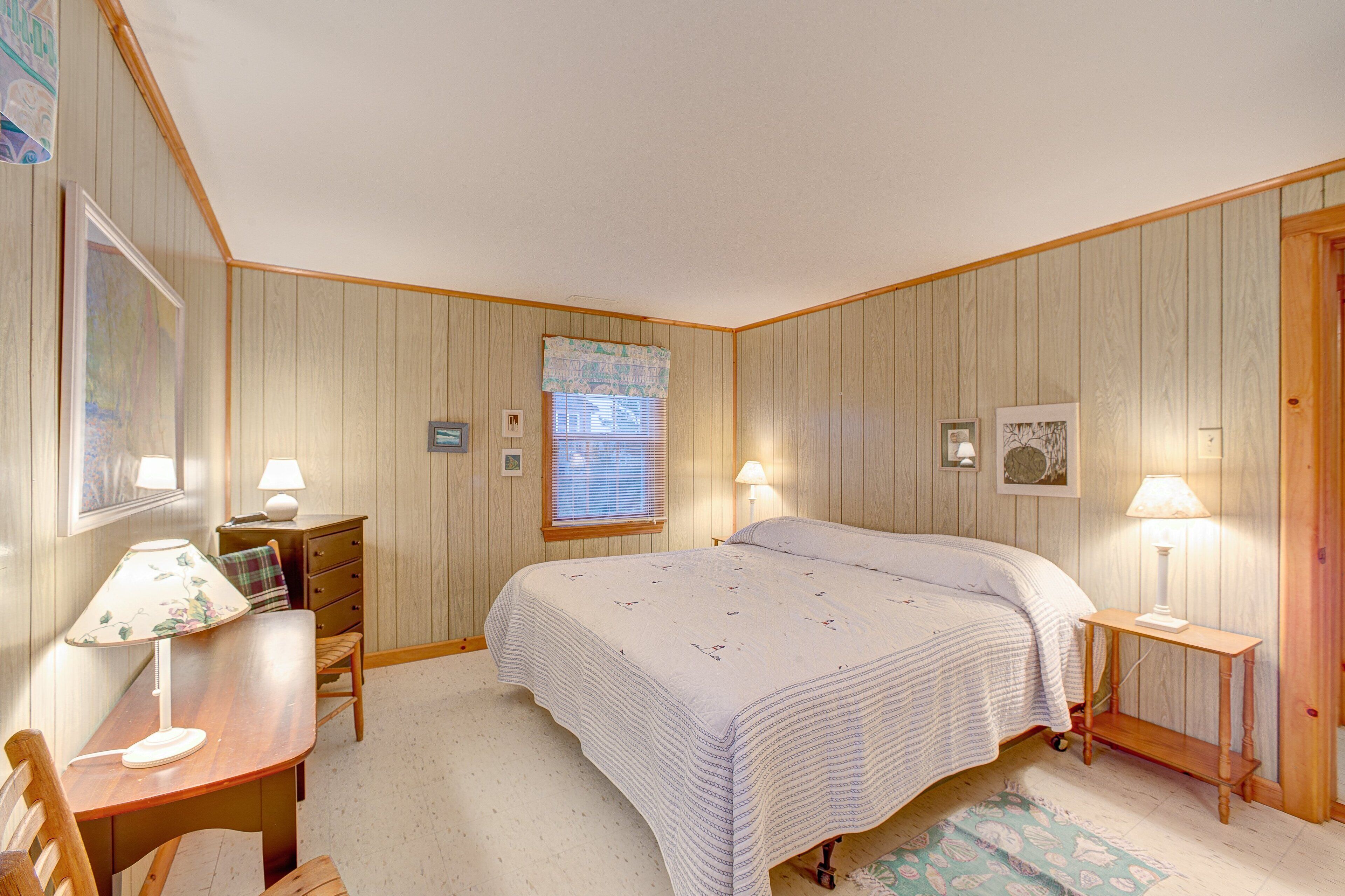 A bedroom with a bed, a desk, a chair, a dresser, and a window with blinds.