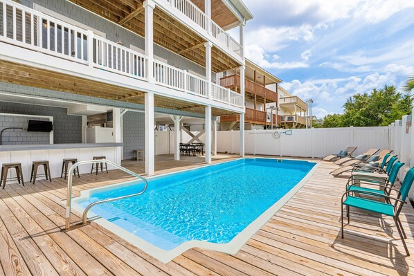 A pool area with a wooden deck, lounge chairs, and a bar area with stools.