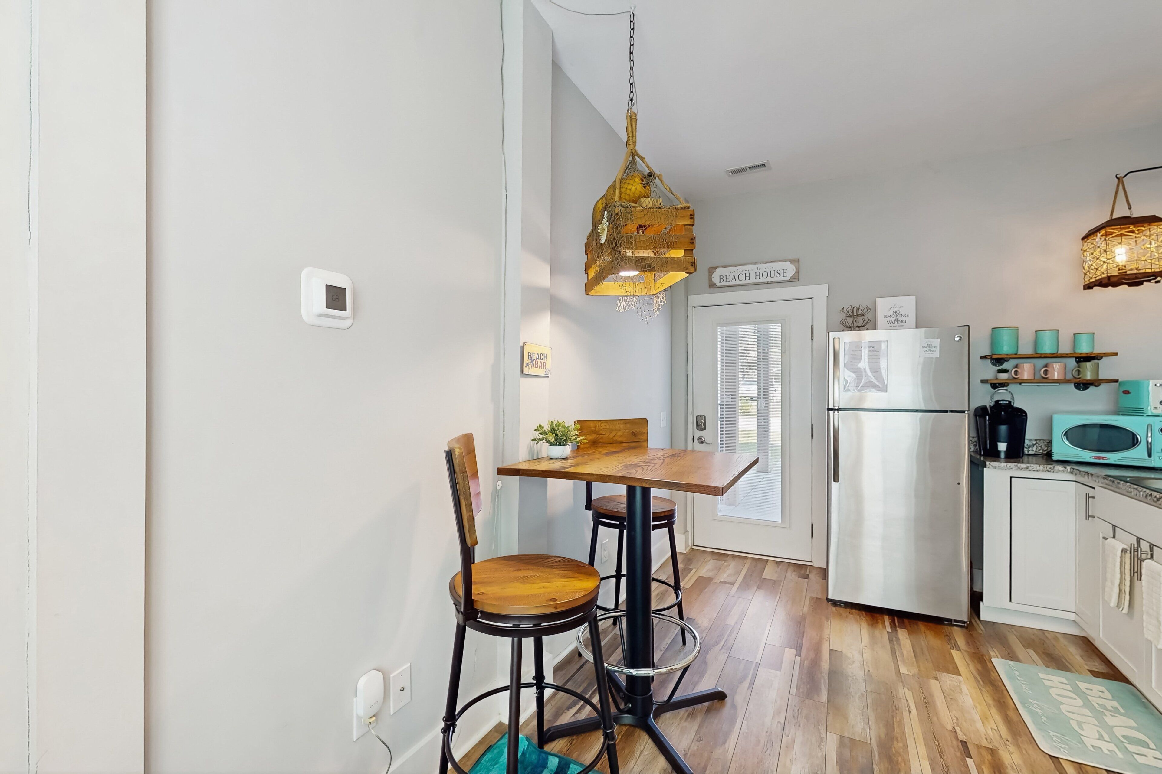 Una cocina compacta con una mesa de madera, dos sillas, una lámpara colgante y un refrigerador.