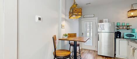 Una cocina compacta con una mesa de madera, dos sillas, una lámpara colgante y un refrigerador.
