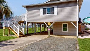 A two-story house with a covered porch and a staircase leading to a deck. - Bright Home with Deck, Patio, High-Speed WiFi, W/D, & Central AC - Near Beach (Holden Beach)