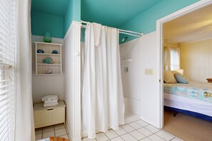 A bathroom with a shower curtain, a toilet, and a sink with a shelf above.