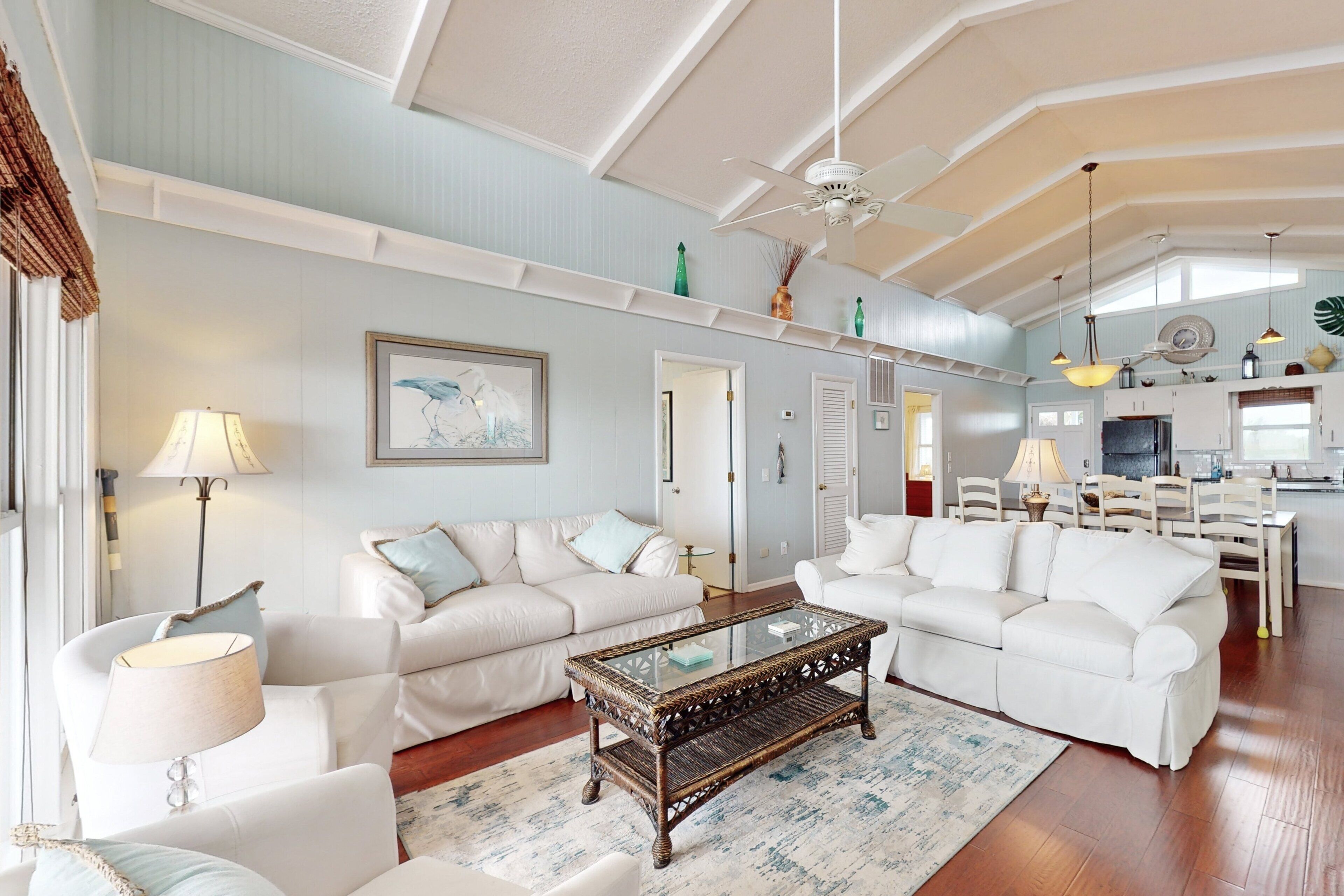 A spacious living room with two white sofas, a glass coffee table, and a dining area with a white table and chairs.