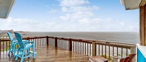A wooden deck with chairs and a table overlooking the ocean.