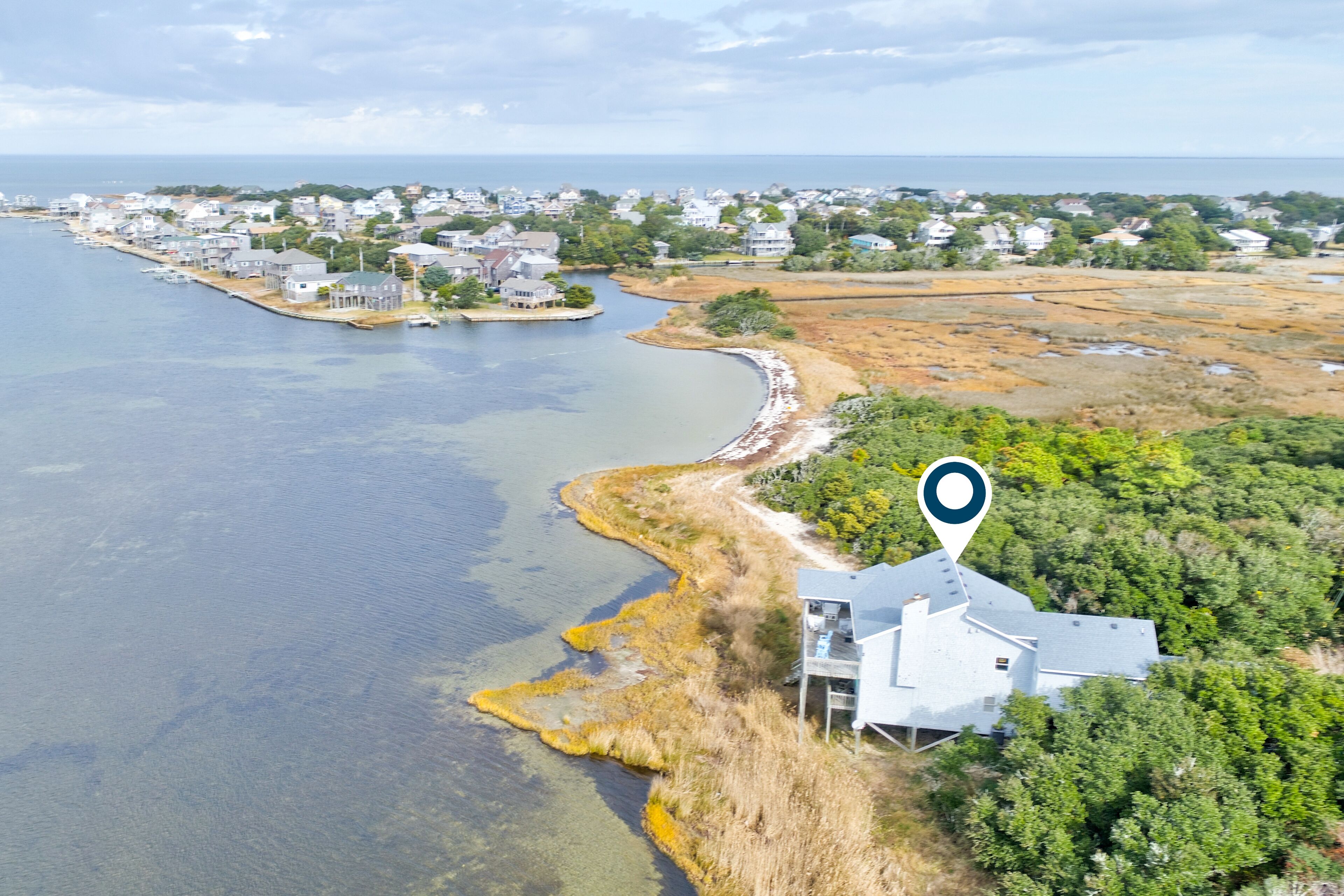 Vista aérea de un pueblo costero con casas a lo largo de la costa, cielo despejado y un marcador de ubicación.