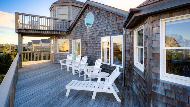 Une terrasse en bois avec des chaises Adirondack blanches et une petite table, offrant une vue sur le paysage urbain.