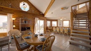 Un intérieur en bois comprenant un coin repas, des chaises, un escalier et une vue dégagée grâce à de grandes fenêtres.