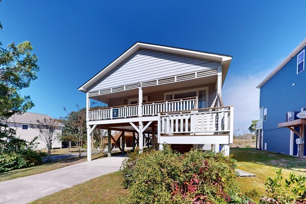 A two-story house with a balcony, a covered porch, and a visible address number. - Marsh-View Escape: Walk to Beach | Marsh-View Escape with Screened Porch & Outdoor Shower (Oak Island)