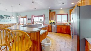 A spacious kitchen with wooden cabinets, a stainless steel refrigerator, and a large island with chairs. - Outer Banks house with private pool, hot tub, W/D & ocean view - dog-friendly (Avon)