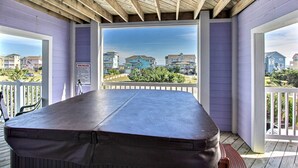 A covered outdoor area with a table and chairs, a view of neighboring houses, and a sign indicating spa rules. - Outer Banks house with private pool, hot tub, W/D & ocean view - dog-friendly (Avon)
