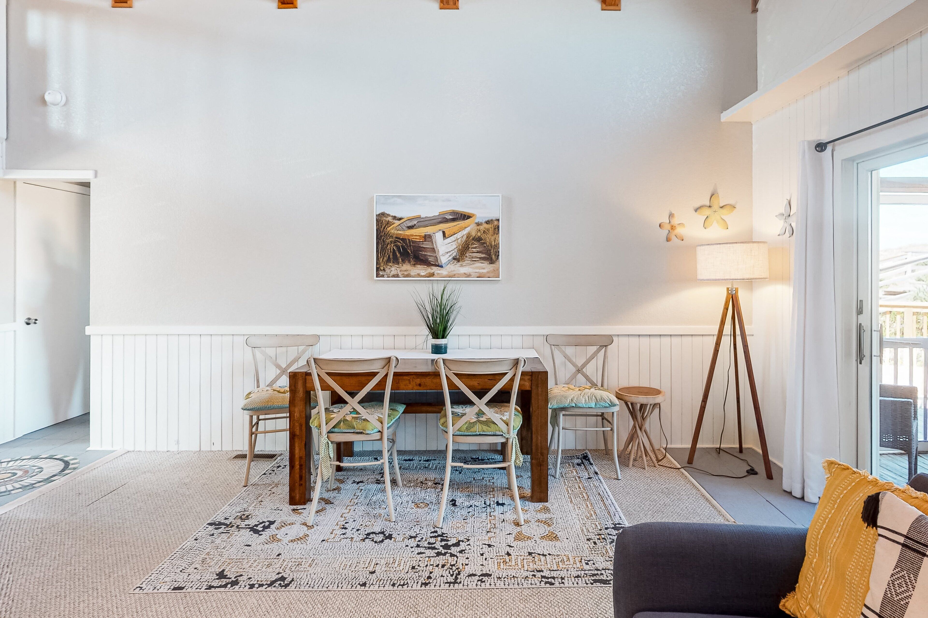 A dining area with a wooden table and chairs, a painting of a boat on the wall, and a lamp.