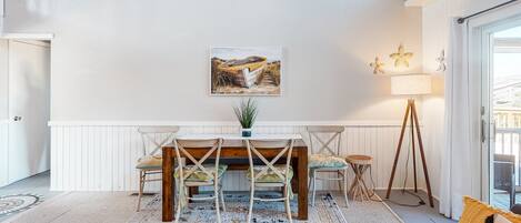 A dining area with a wooden table and chairs, a painting of a boat on the wall, and a lamp.