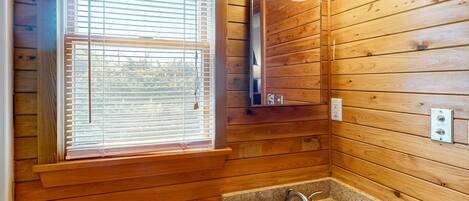 A wooden cabin bathroom with a sink, mirror, and window with blinds.