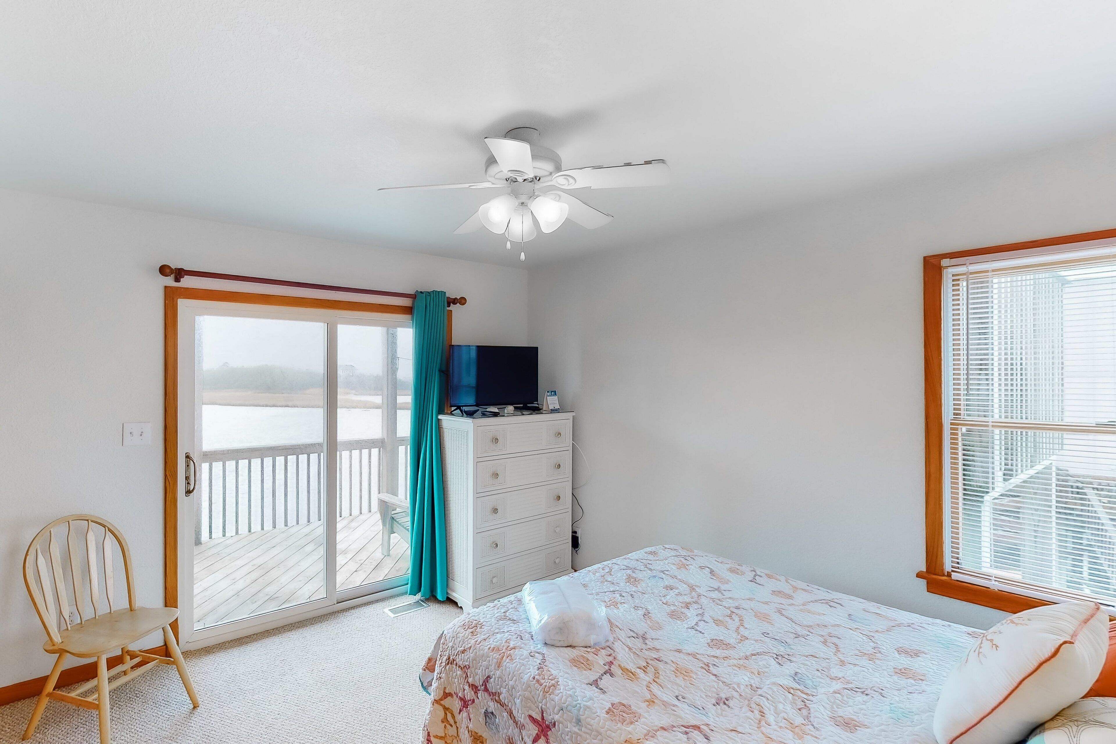 A bedroom with a bed, a dresser, a chair, a ceiling fan, and a sliding glass door leading to a balcony.