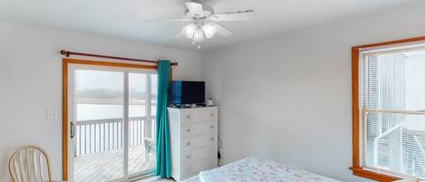 A bedroom with a bed, a dresser, a chair, a ceiling fan, and a sliding glass door leading to a balcony.