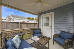 A covered porch with wicker furniture, a glass table, and a view of a house with a sign reading 'HOT ROD'.