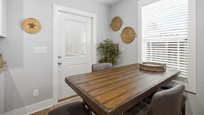 Un comedor con una mesa de madera, sillas, una planta en maceta y una puerta con un reloj de pared circular.