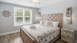 Un dormitorio con cama, ventilador de techo, ventana con persianas y mesita de noche con una linterna.