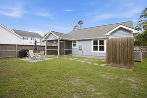 A residential backyard with a covered patio, a grill, and a wooden fence.