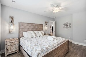 A bedroom with a large bed, a wooden headboard, a nightstand, a wall-mounted lamp, and a ceiling fan.