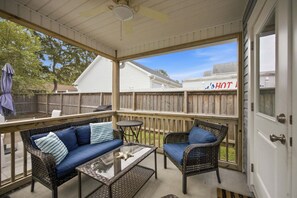A covered outdoor patio with wicker furniture, a glass table, and a view of a house with a 'HOT' sign. - Oak Island Gem: Delightful getaway near the beach with fast WiFi, gas grill, outdoor shower (Oak Island)