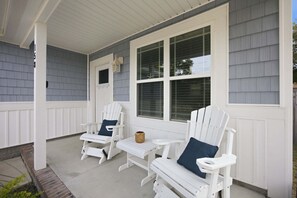 Un portico riparato con due poltrone Adirondack e un tavolino, con una finestra dotata di persiane.