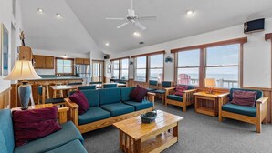 A spacious living area with a sofa, chairs, and a coffee table. There is a kitchen area with wooden cabinets and a refrigerator. - Waterfront home with private hot tub, windsurf launch, amazing view, pool access (Avon)