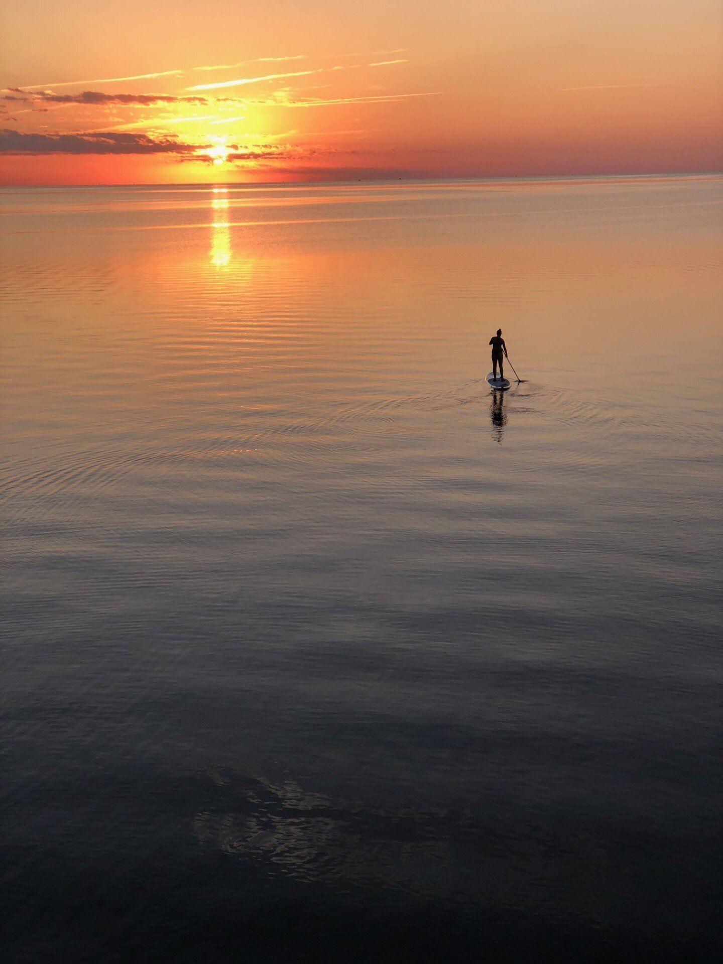 Iemand staat op een paddleboard op een rustig wateroppervlak tijdens de zonsondergang.
