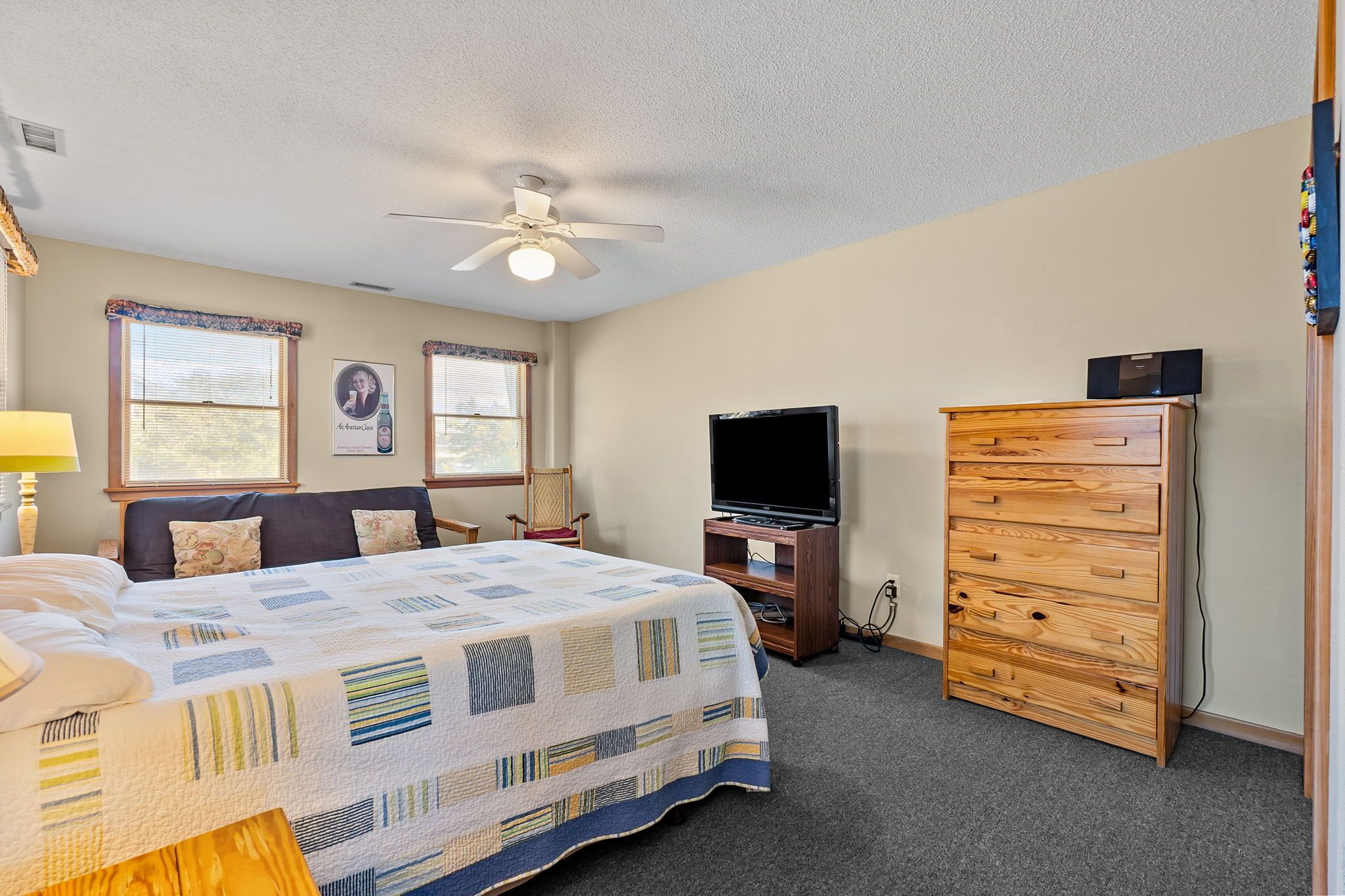 A bedroom with a bed, a dresser, a television, and a ceiling fan.