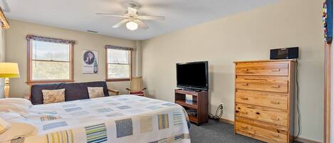 A bedroom with a bed, a dresser, a television, and a ceiling fan.