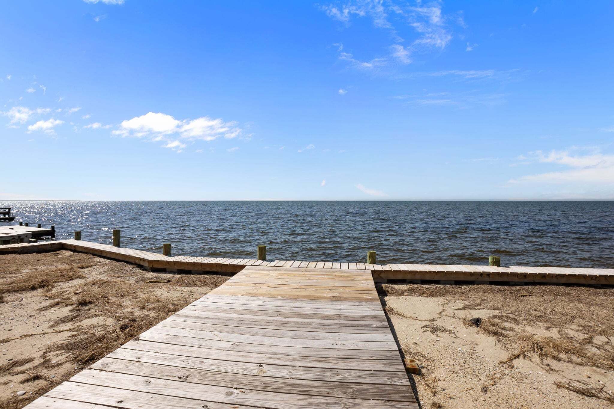 Een houten steiger die uitkomt op een zandstrand, met een kalme zee onder een heldere lucht.