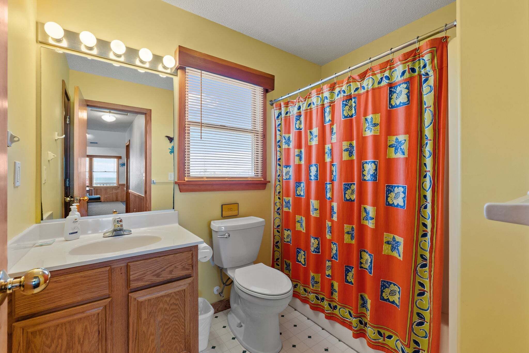 Une salle de bain avec un lavabo blanc, des meubles en bois, des toilettes et un rideau de douche à motifs floraux.