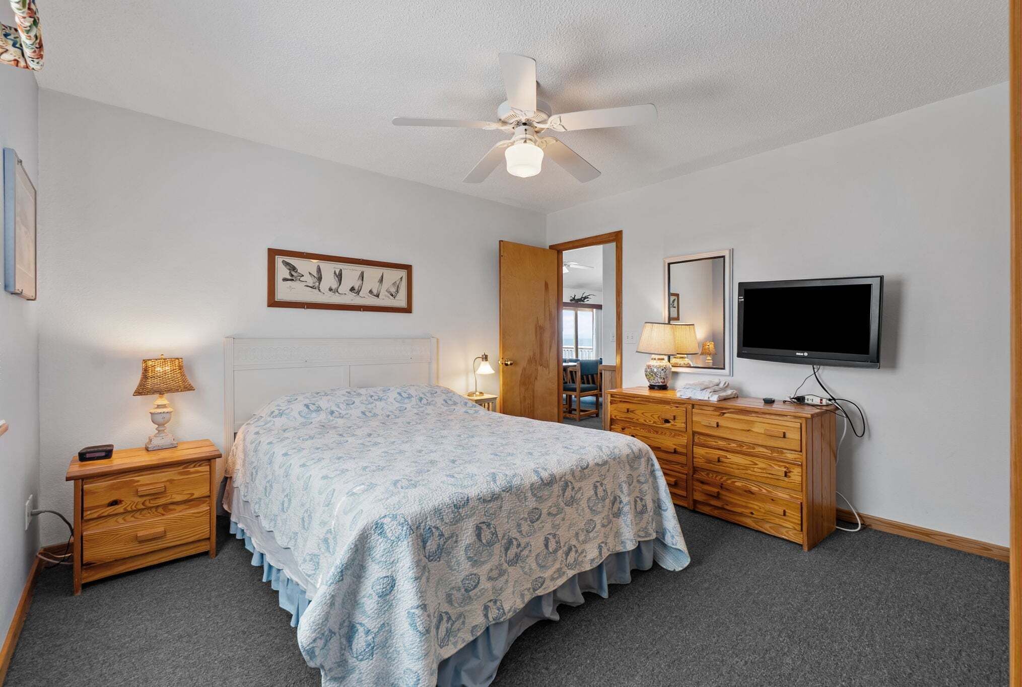 Ein Schlafzimmer mit Bett, Holzkommode, Fernseher und Deckenventilator.