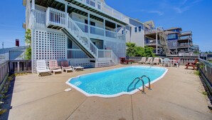 Ein Poolbereich mit klarem, blauem Pool, weißen Liegestühlen und einer Holzterrasse mit einer Treppe zu einem Balkon.