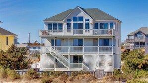Ein zweistöckiges Strandhaus mit Balkon, Treppe und Blick auf den Ozean.