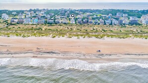 Luftaufnahme einer Küstenwohngegend mit Strandhäusern, einem Sandstrand und Wellen.