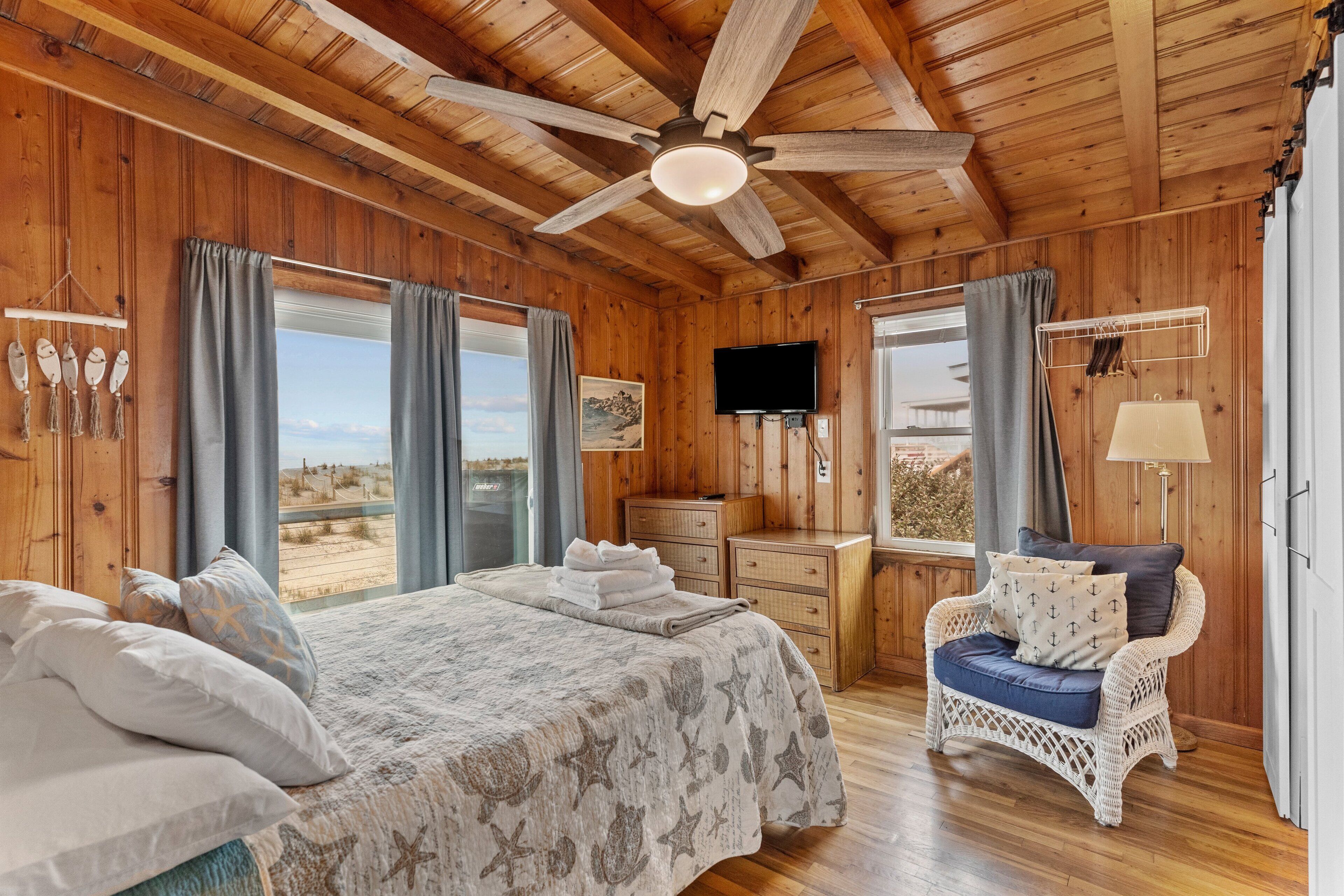 Een houten slaapkamer met een bed, een stoel, een televisie en een raam met gordijnen.