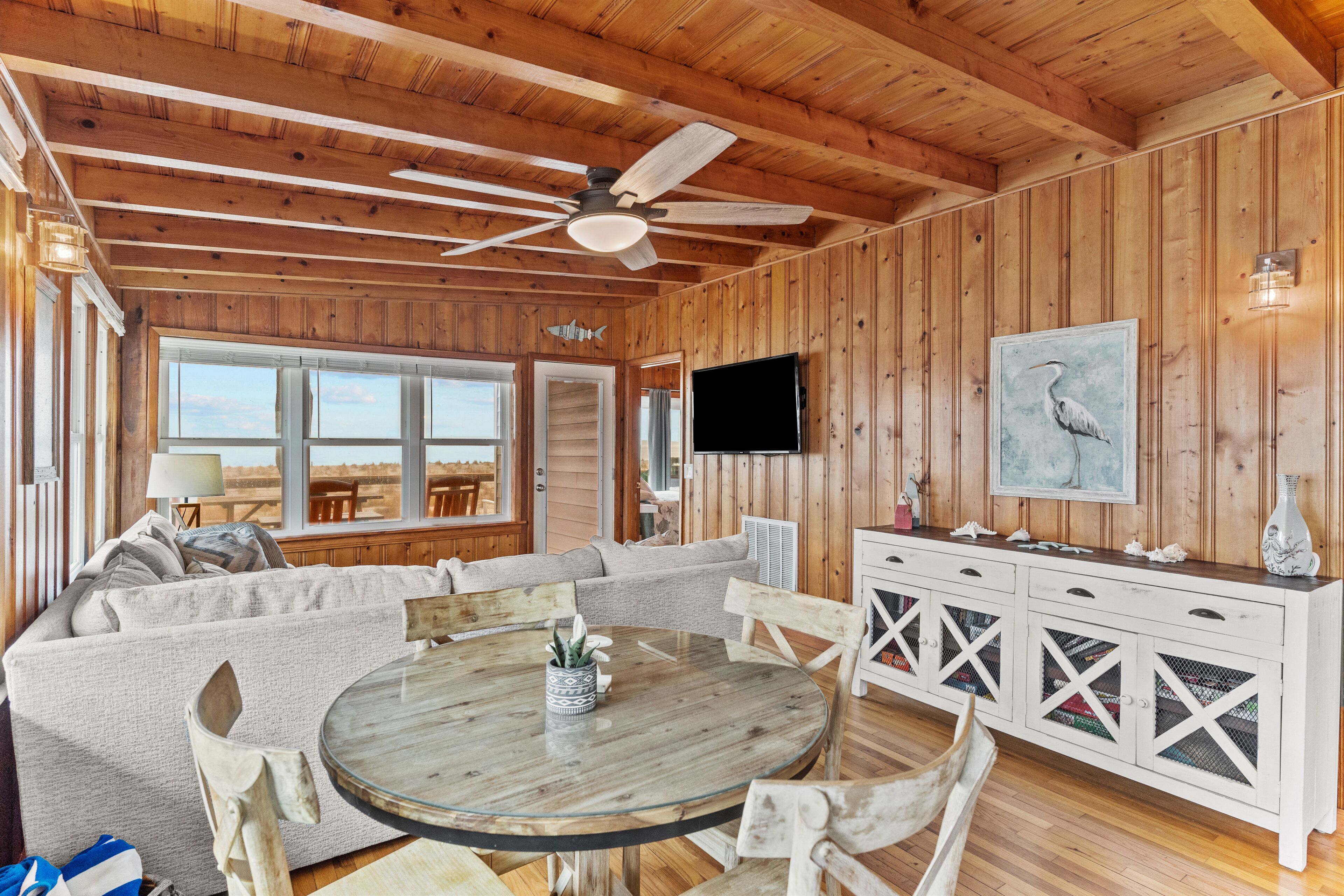 A wooden interior with a round dining table, a sofa, and a TV mounted on the wall.