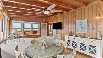 A wooden interior with a round dining table, a sofa, and a TV mounted on the wall.