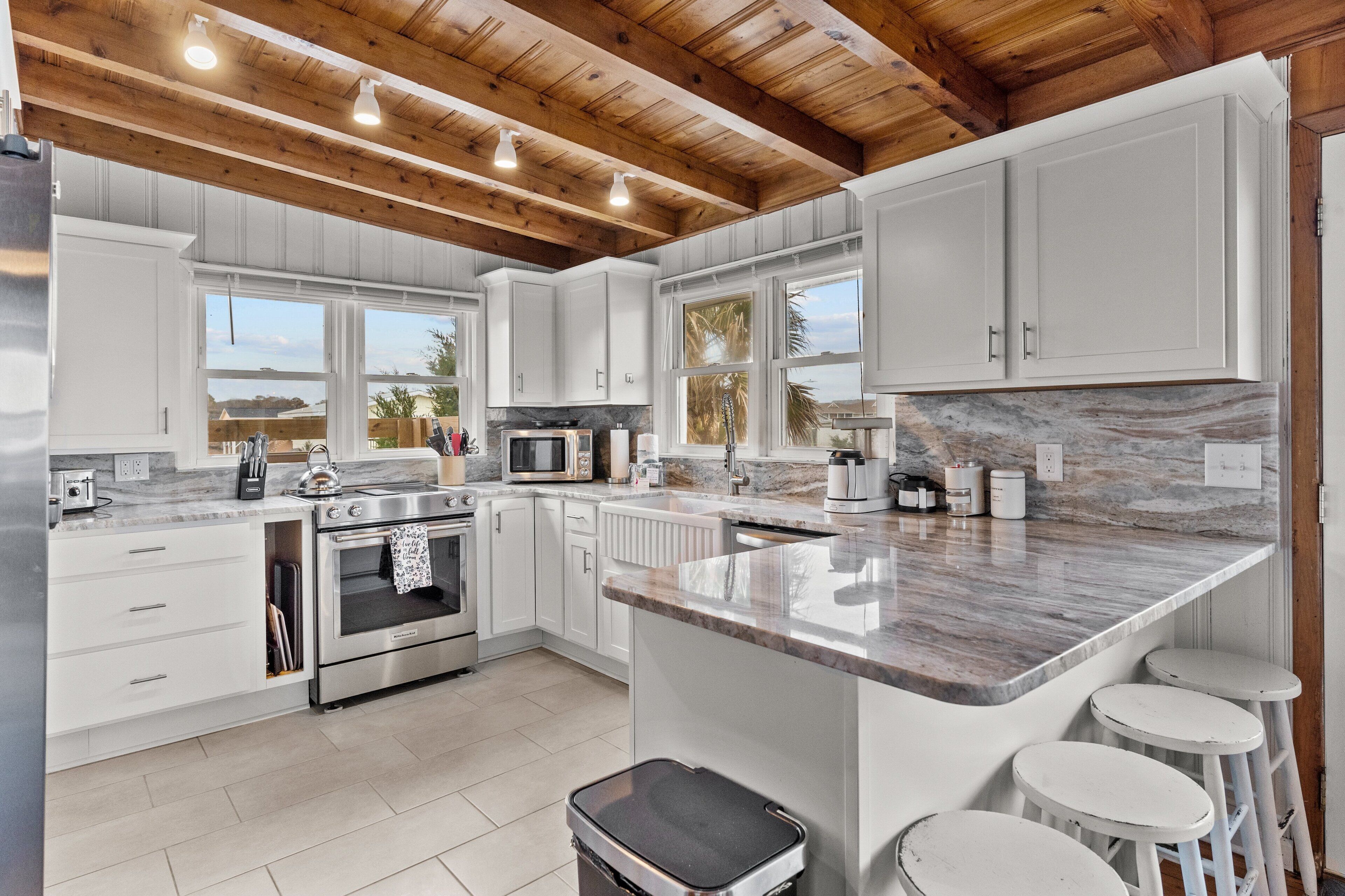 A modern kitchen with white cabinets, a marble countertop, and a wooden ceiling.