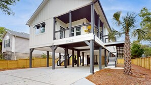 Ein modernes, zweistöckiges Haus mit überdachter Veranda, einer Treppe, die zum Obergeschoss führt, und einer kleinen Außenbereich-Sitzgelegenheit.
