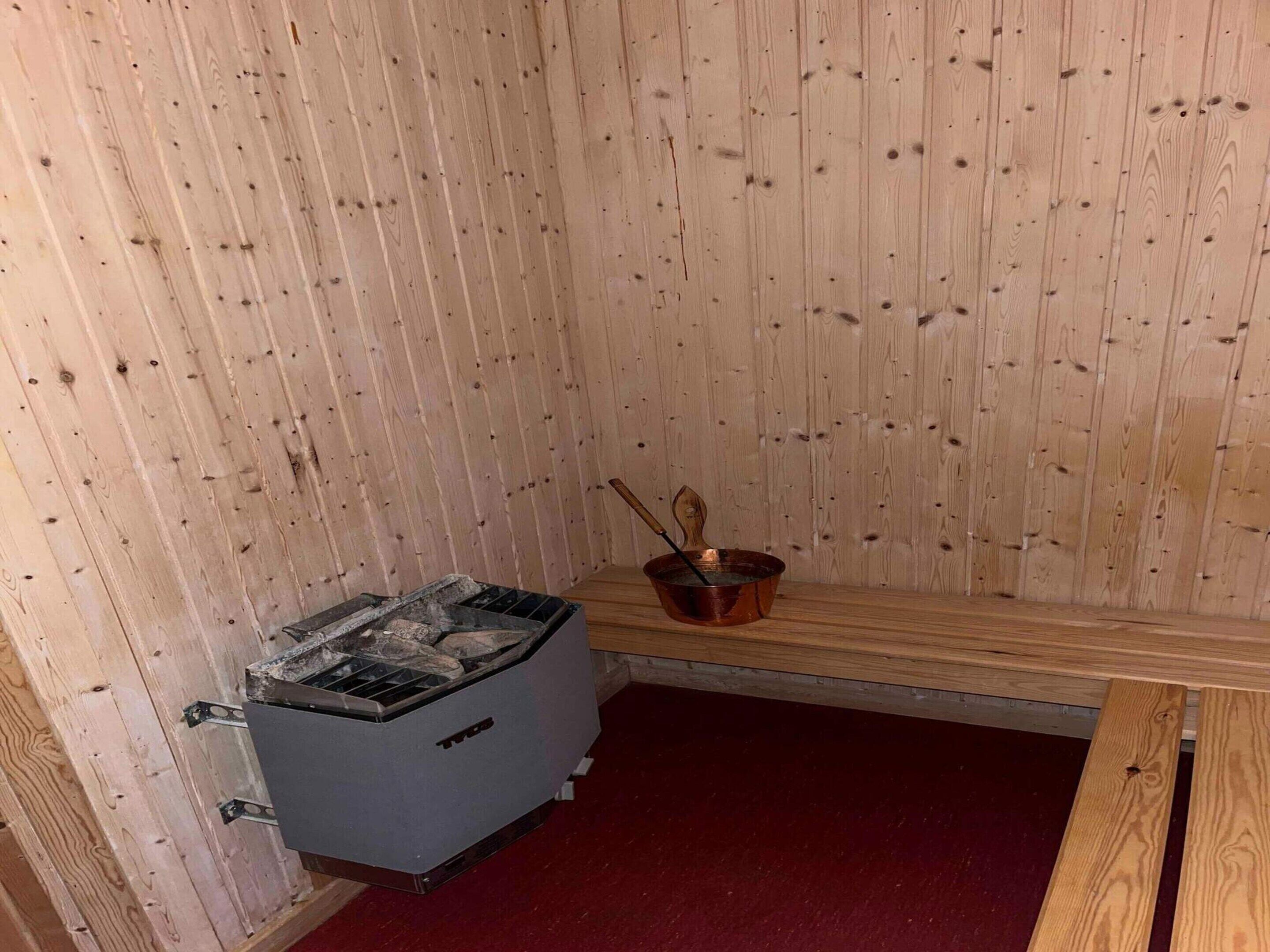 A sauna room with a wooden wall, a sauna unit, a copper bucket, and a wooden bench.
