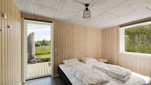 A bedroom with a bed, a nightstand, a window, and a door leading to an outdoor deck. - 5 Star Holiday Home in Allinge (Allinge)
