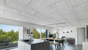 A modern kitchen with a central island, large windows, and a dining area with chairs and a table. - 5 Star Holiday Home in Allinge (Allinge)
