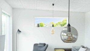 A modern living room with a clear view of the outdoors through a window, a grey sofa, a black armchair, and a coffee table. - 5 Star Holiday Home in Allinge (Allinge)