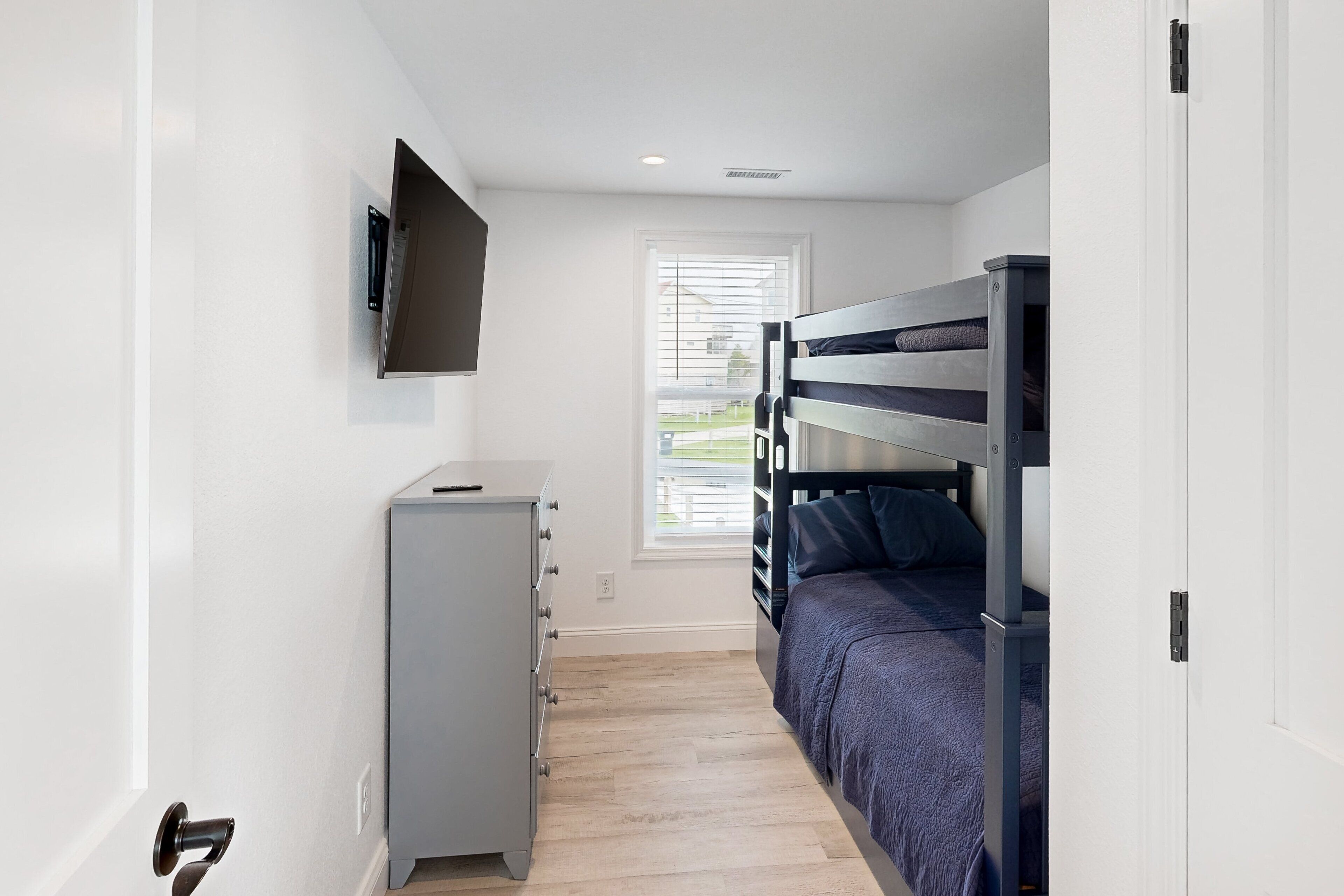 A bedroom with a bunk bed, a dresser, and a TV mounted on the wall.