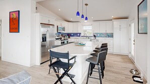 A modern kitchen with a large island, white cabinetry, and blue pendant lights.