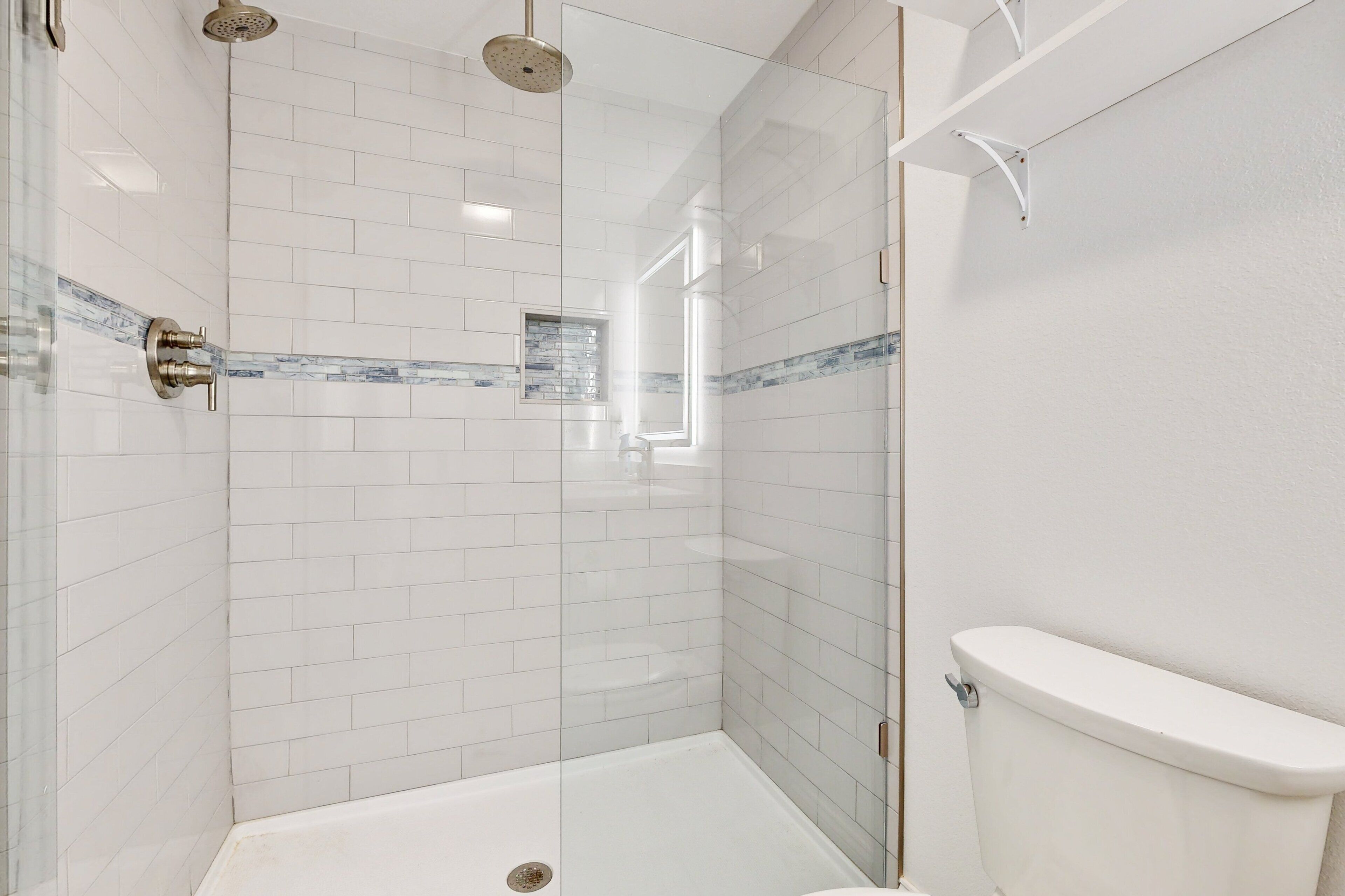 A modern bathroom with white subway tiles, a glass shower enclosure, and a white toilet.