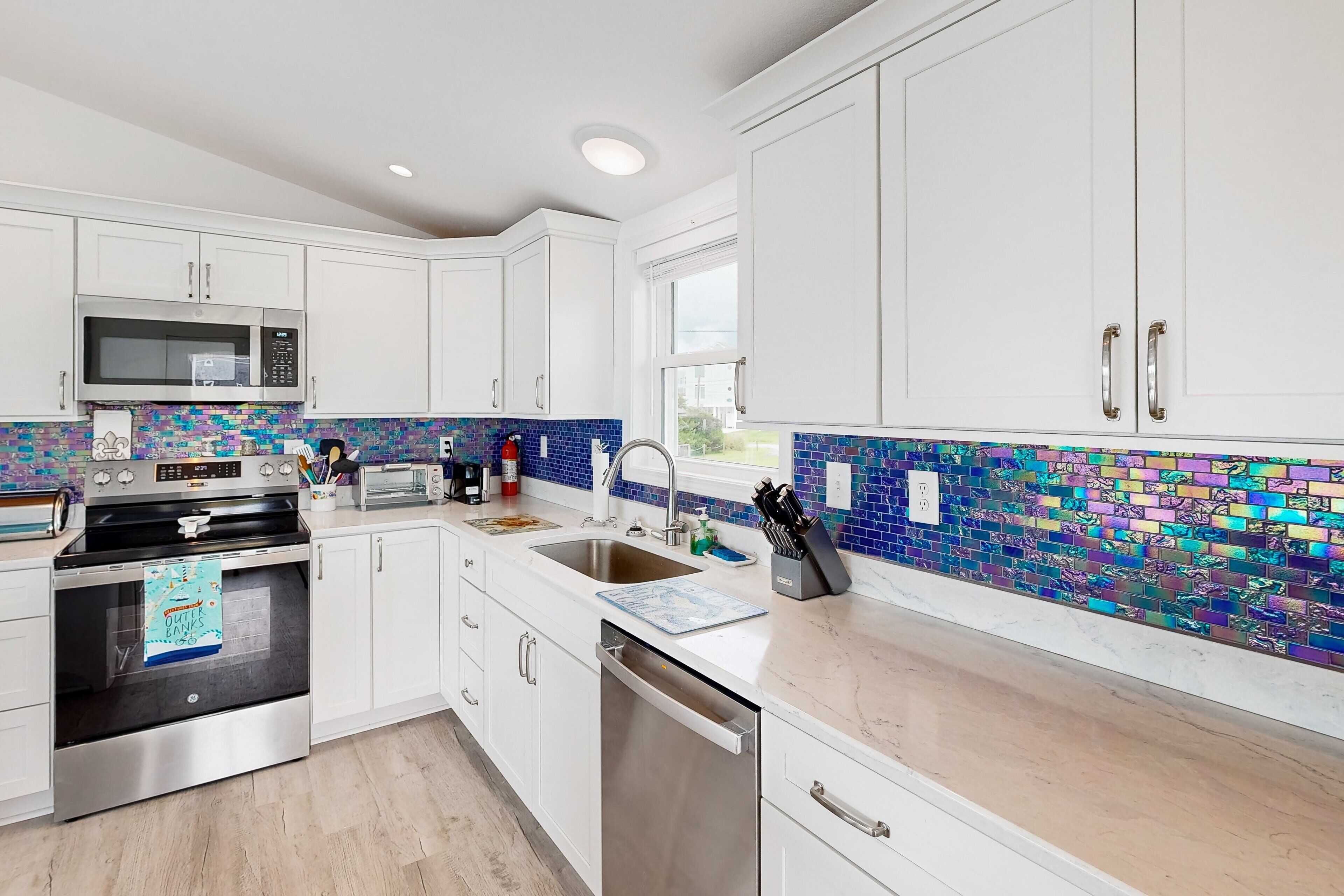 A modern kitchen with white cabinets, stainless steel appliances, and colorful mosaic backsplash.