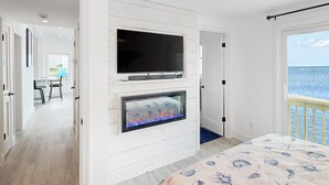 A room with a fireplace, a television, and a view of the ocean.